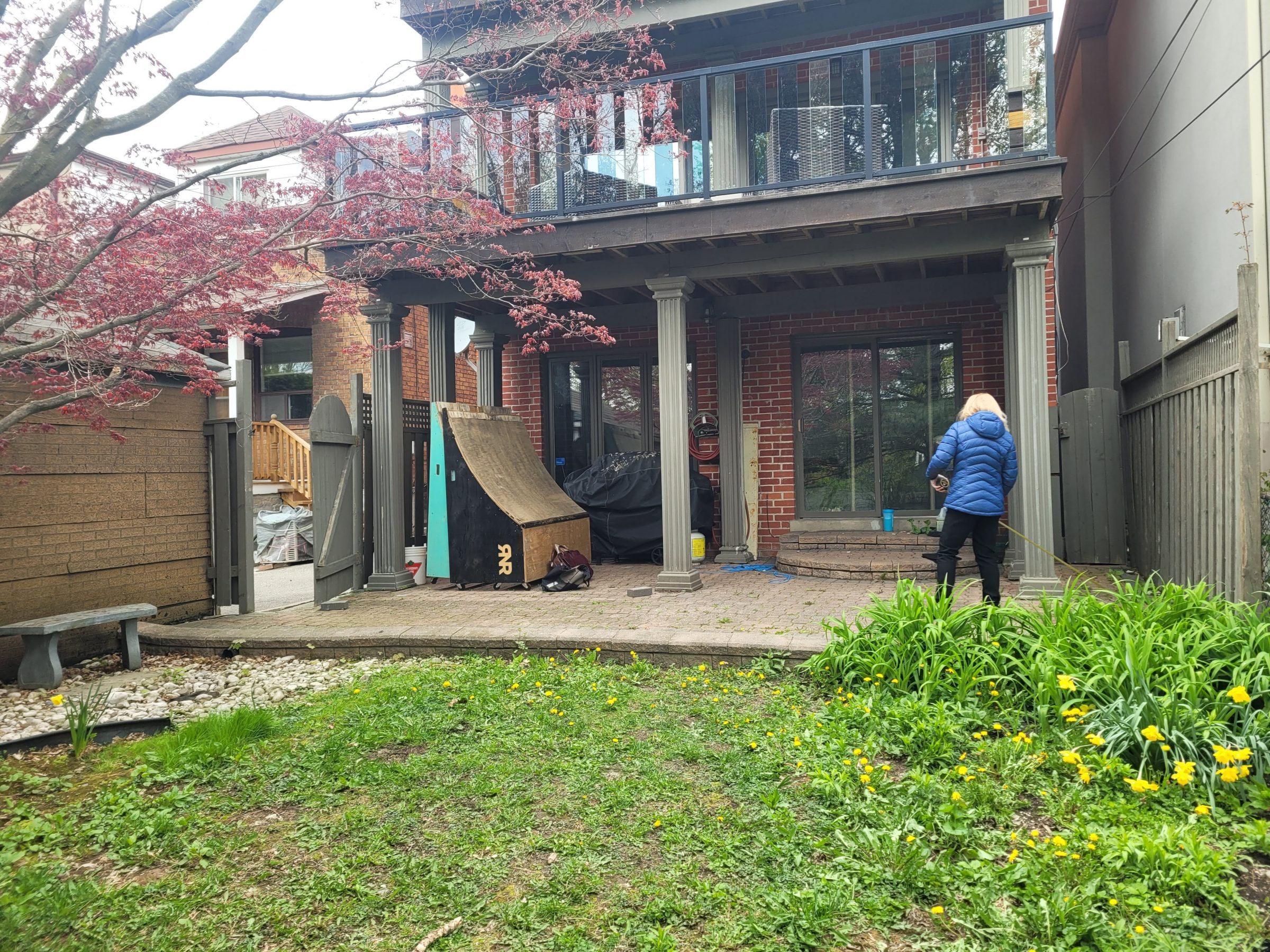 Person gardening in backyard with deck and flowers.