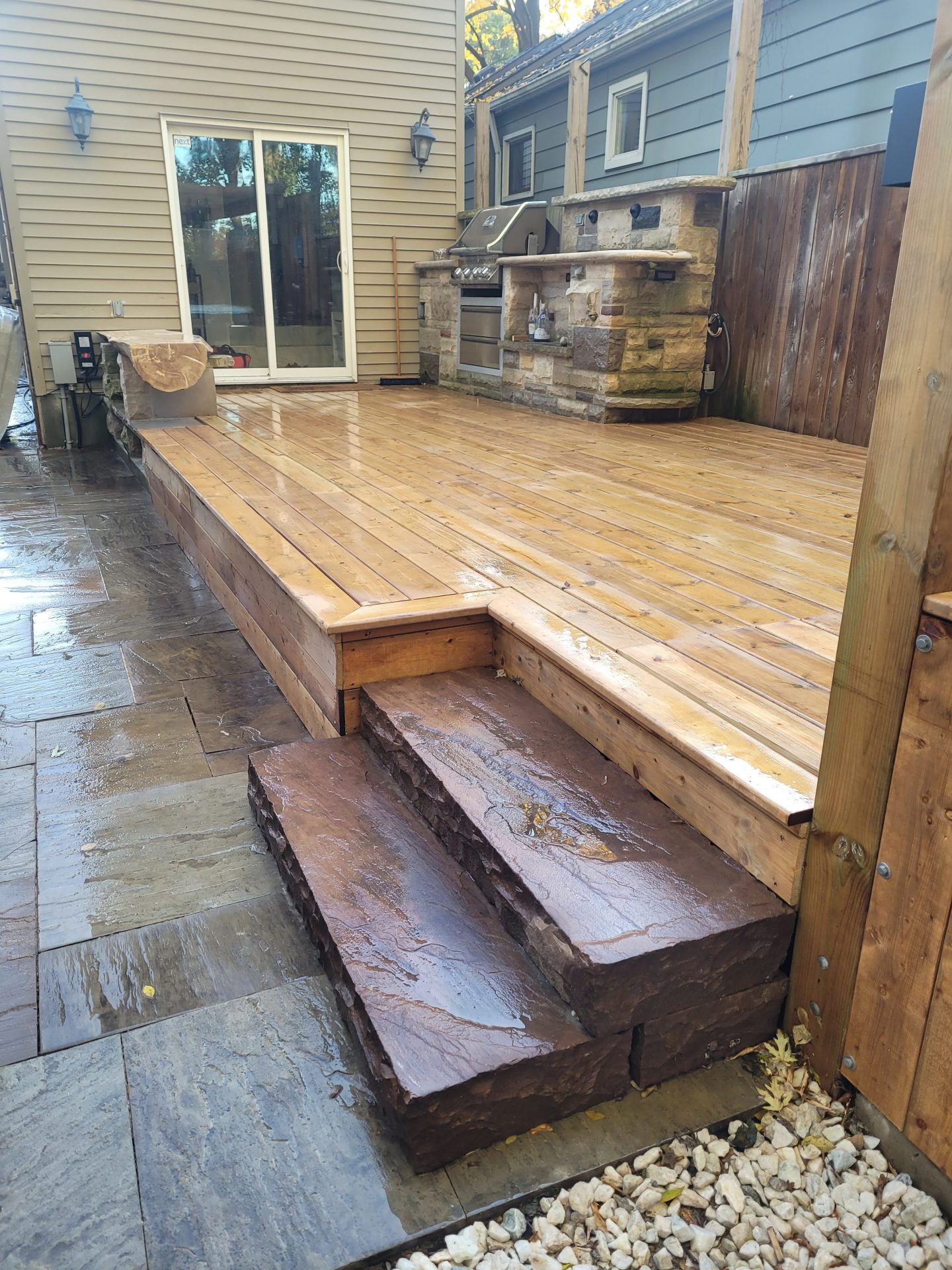 Wooden deck with stone steps and outdoor kitchen.