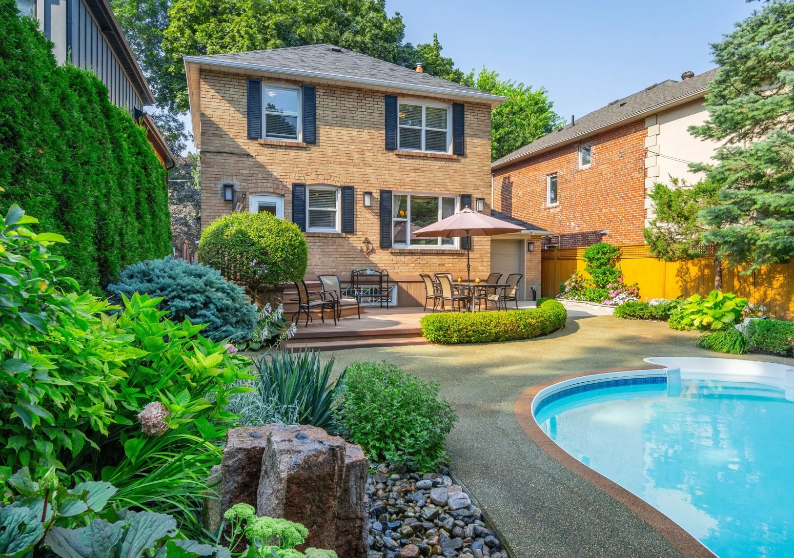 Backyard with patio, pool, greenery, and two-story house.