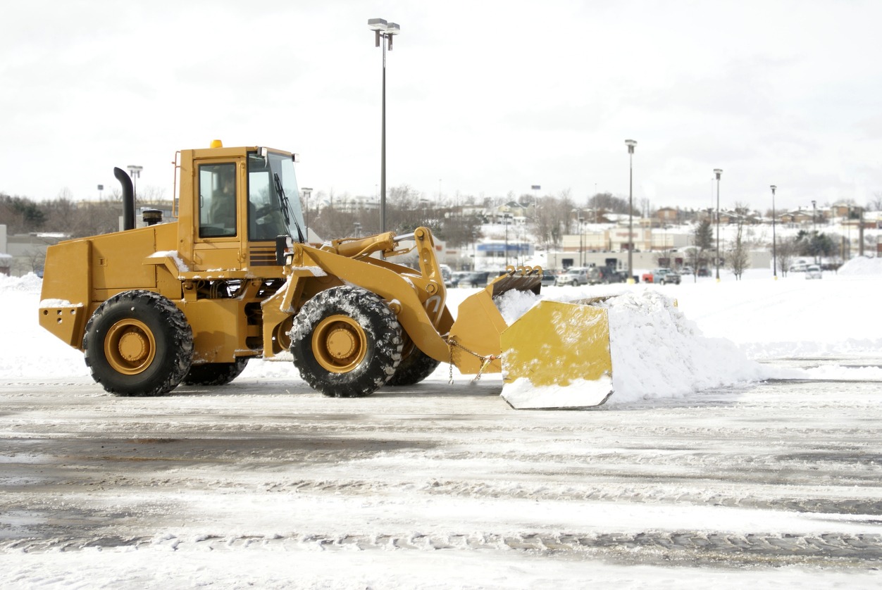 Yellow snowplow clearing a snowy parking lot.