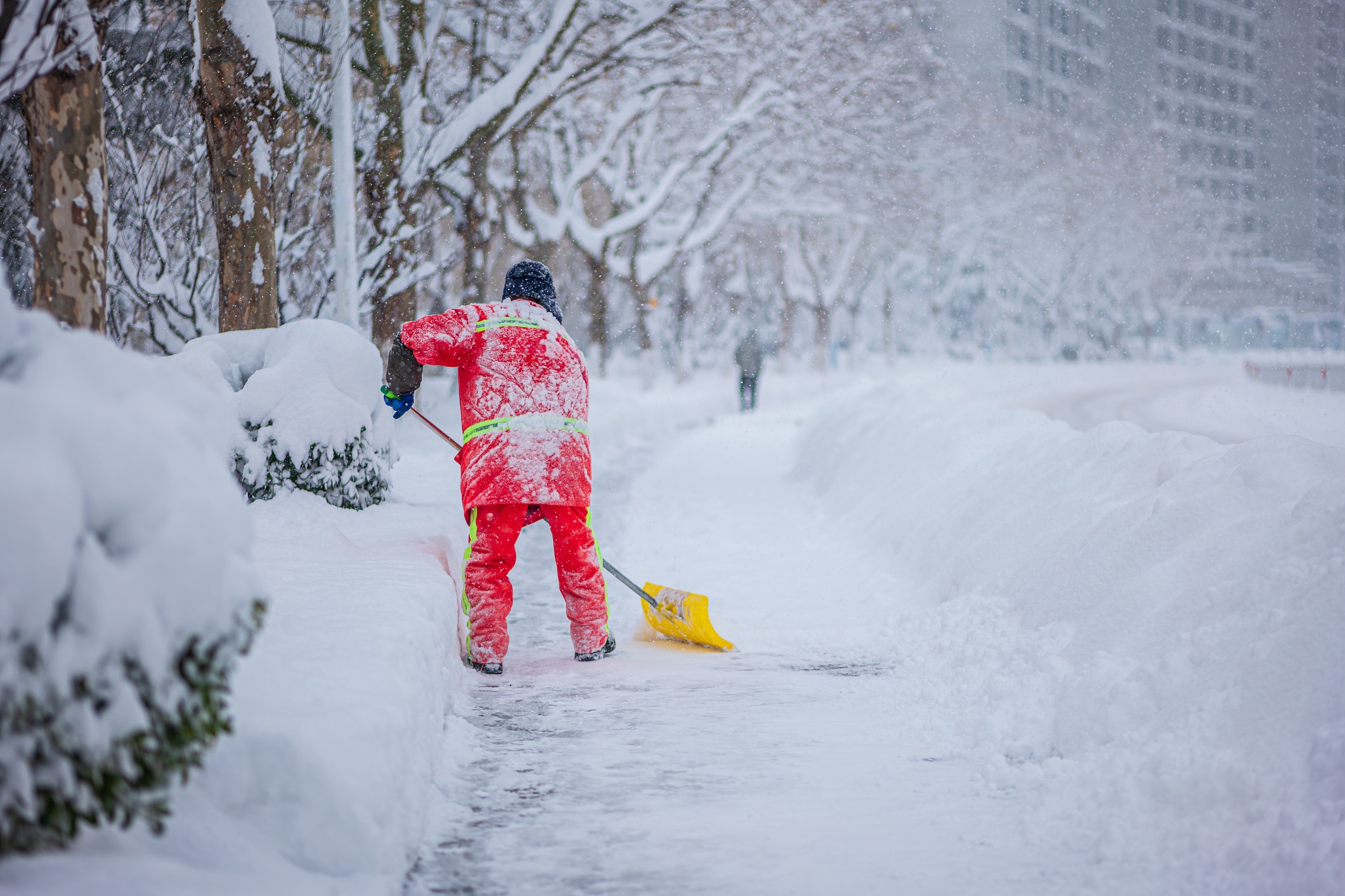 Person shoveling snow on a city sidewalk.